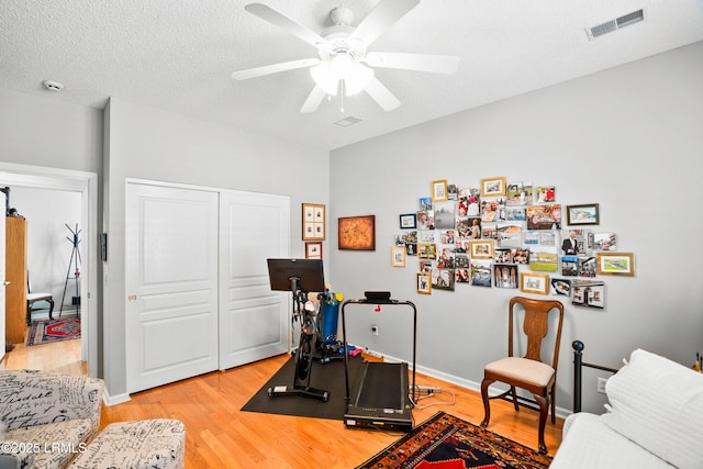 workout room featuring ceiling fan, a textured ceiling, and light hardwood / wood-style floors