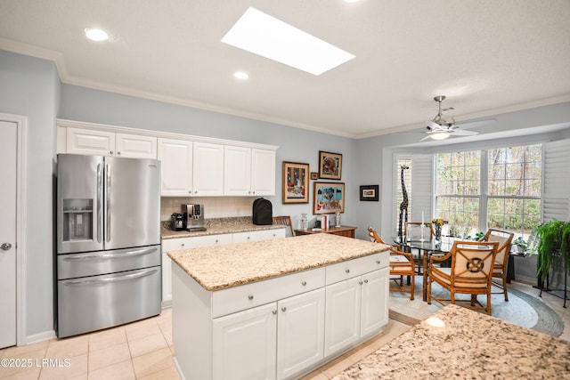 kitchen featuring stainless steel refrigerator with ice dispenser, a kitchen island, white cabinets, and a skylight