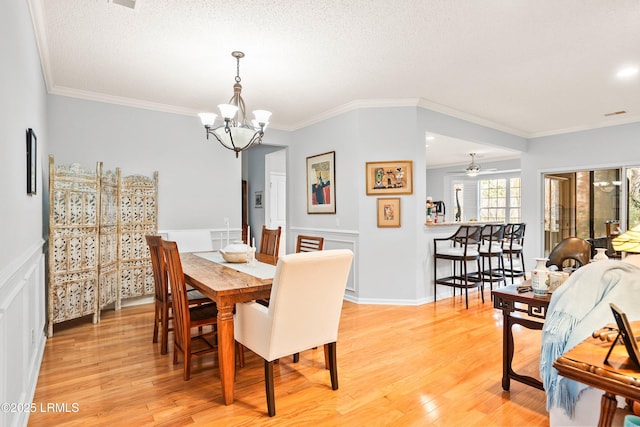 dining space with crown molding, ceiling fan with notable chandelier, light hardwood / wood-style flooring, and a textured ceiling