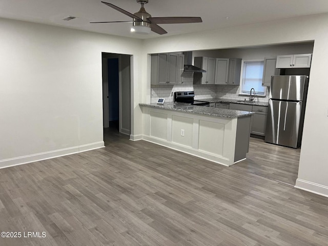 kitchen featuring wall chimney exhaust hood, stainless steel refrigerator, gray cabinets, kitchen peninsula, and electric stove