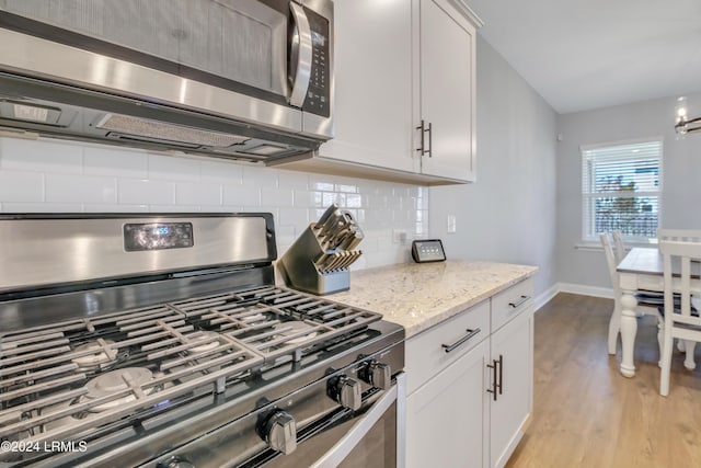 kitchen featuring stainless steel appliances, white cabinetry, light stone countertops, and decorative backsplash