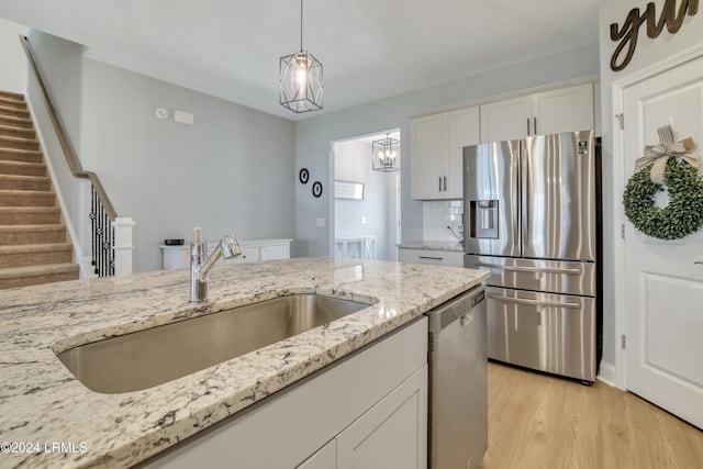 kitchen with sink, white cabinetry, light stone counters, light wood-type flooring, and stainless steel appliances