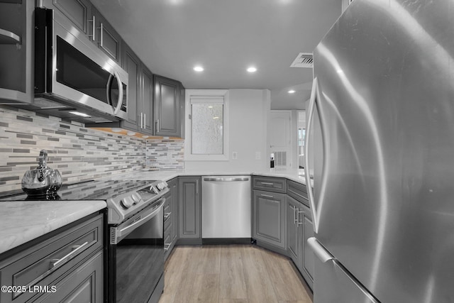 kitchen featuring appliances with stainless steel finishes, tasteful backsplash, gray cabinetry, light stone counters, and light hardwood / wood-style floors