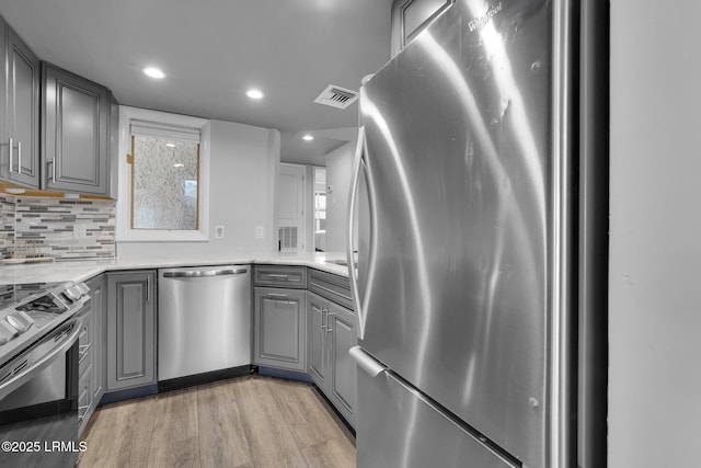 kitchen with light stone counters, light hardwood / wood-style flooring, gray cabinets, stainless steel appliances, and decorative backsplash