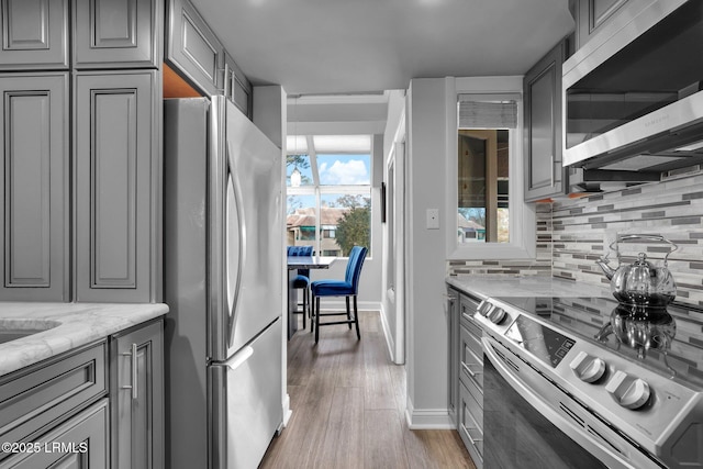 kitchen featuring appliances with stainless steel finishes, gray cabinetry, backsplash, light stone countertops, and light hardwood / wood-style floors