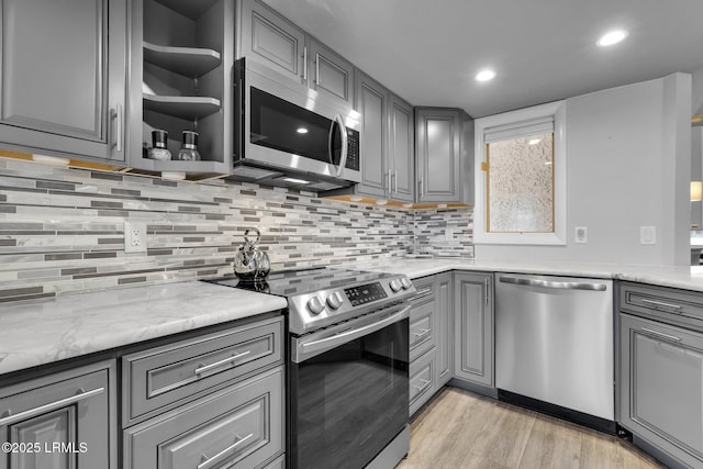 kitchen with gray cabinets, light stone countertops, appliances with stainless steel finishes, and backsplash