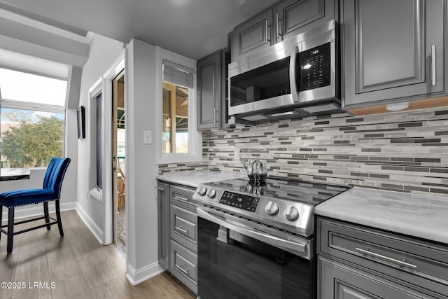 kitchen featuring appliances with stainless steel finishes, gray cabinetry, backsplash, and light hardwood / wood-style floors