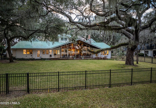 back of property featuring a fenced backyard, a chimney, metal roof, and a lawn