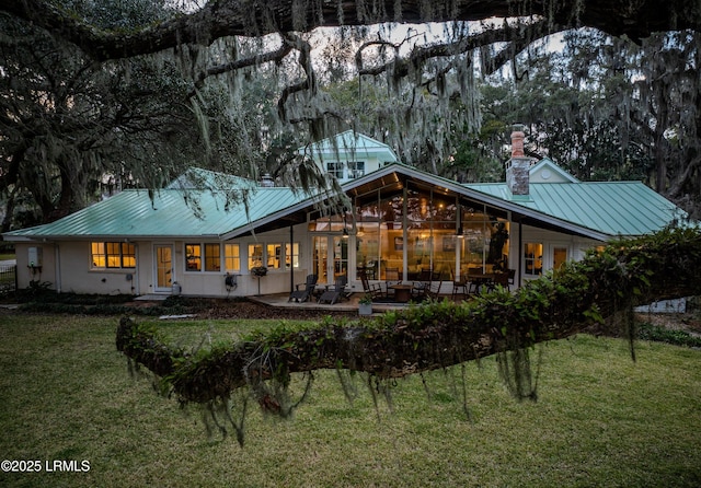 rear view of house featuring a standing seam roof, metal roof, a lawn, a chimney, and a patio area