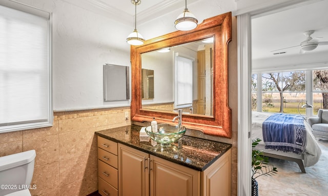 half bath featuring crown molding, tile walls, toilet, a ceiling fan, and vanity