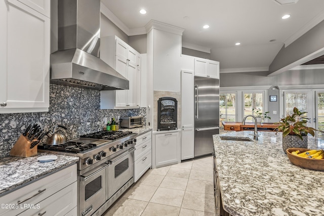 kitchen featuring wall chimney range hood, ornamental molding, high end appliances, and a sink