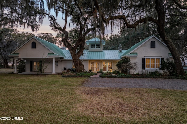 view of front of home featuring covered porch, a yard, a chimney, and metal roof