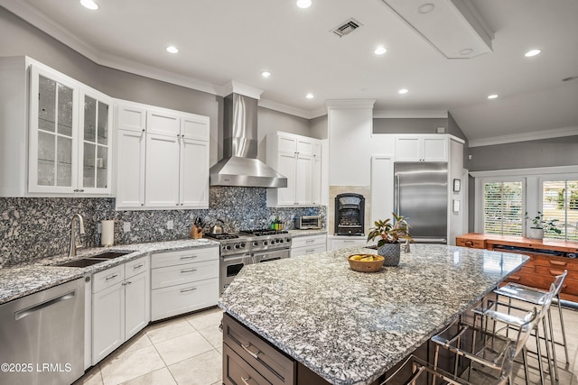 kitchen featuring visible vents, premium appliances, wall chimney exhaust hood, a center island, and a sink