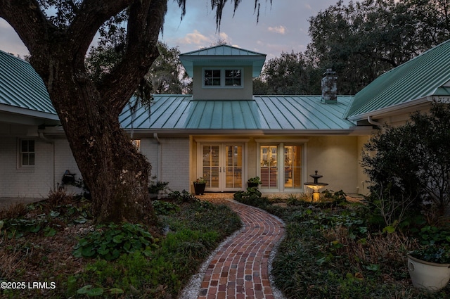 exterior space featuring a chimney, metal roof, a standing seam roof, french doors, and brick siding