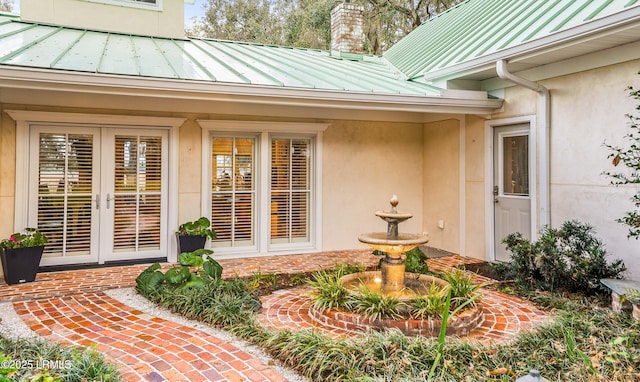 property entrance with french doors, a chimney, stucco siding, a standing seam roof, and metal roof