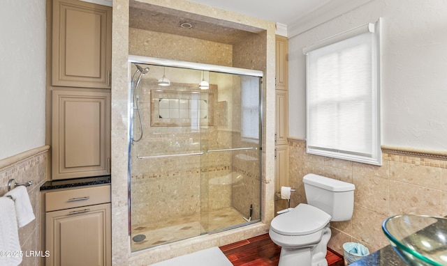 bathroom with tile walls, wainscoting, a shower stall, and toilet