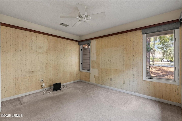 empty room with carpet floors, a ceiling fan, visible vents, and a textured ceiling