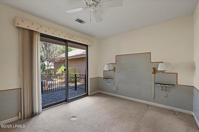 spare room featuring a wainscoted wall, carpet, visible vents, and a textured ceiling