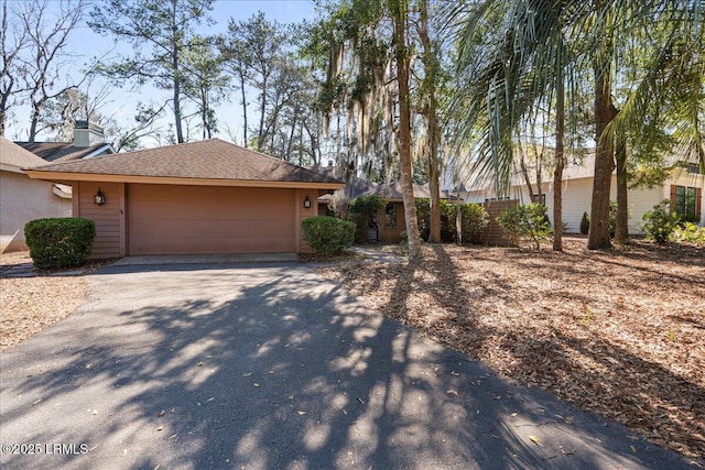 single story home featuring aphalt driveway, a chimney, an attached garage, and a shingled roof