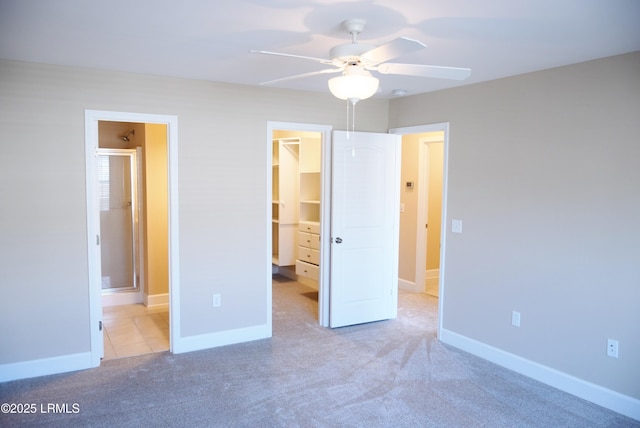 unfurnished bedroom with ensuite bathroom, a walk in closet, light carpet, a closet, and ceiling fan