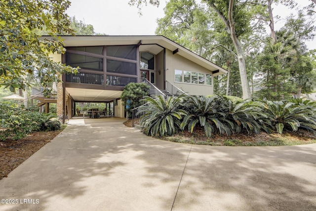 view of front of house featuring a carport, stairway, driveway, and a sunroom