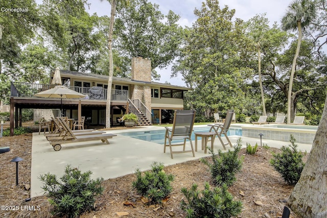 outdoor pool featuring a patio area, a wooden deck, stairs, and a diving board