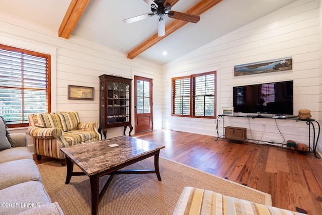 living room featuring hardwood / wood-style flooring, vaulted ceiling with beams, ceiling fan, and wood walls