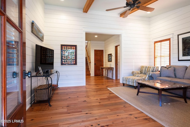 living room with ceiling fan, hardwood / wood-style flooring, beamed ceiling, and wood walls