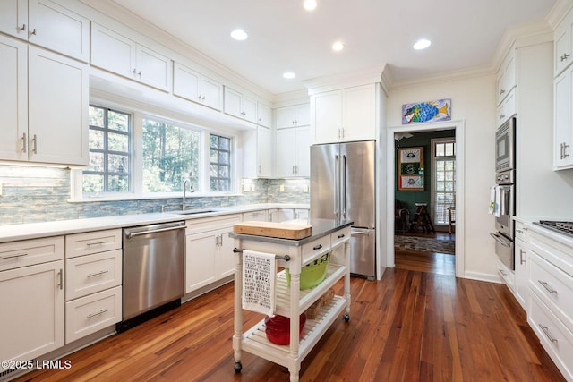 kitchen with sink, appliances with stainless steel finishes, white cabinetry, ornamental molding, and dark hardwood / wood-style flooring