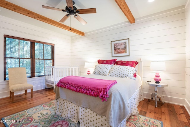 bedroom featuring hardwood / wood-style floors, beamed ceiling, ceiling fan, and wood walls