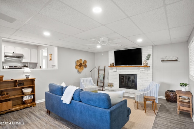 living room with a brick fireplace, hardwood / wood-style flooring, a paneled ceiling, and ceiling fan