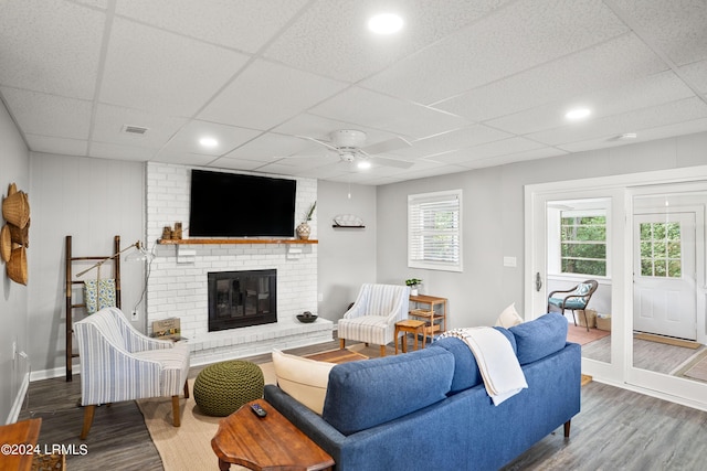 living room featuring a drop ceiling, hardwood / wood-style flooring, a fireplace, and ceiling fan