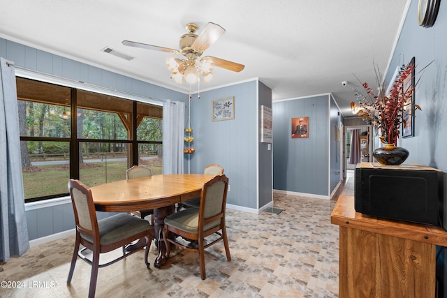 dining room featuring ceiling fan, ornamental molding, wooden walls, and a wealth of natural light