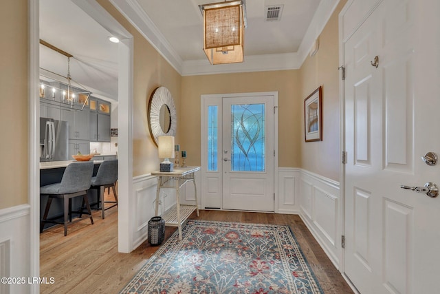 foyer featuring ornamental molding, wainscoting, wood finished floors, and visible vents