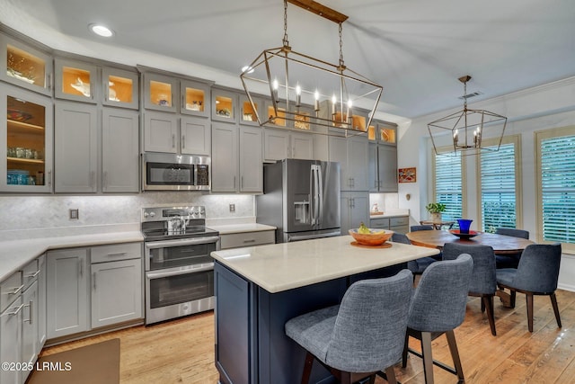 kitchen featuring decorative backsplash, a breakfast bar, stainless steel appliances, gray cabinetry, and a chandelier