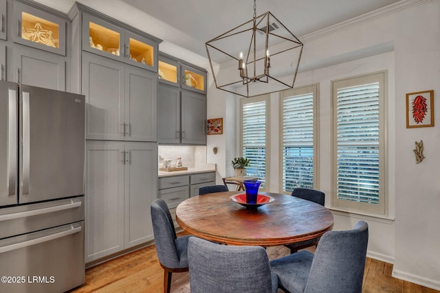 dining area featuring light wood-style floors, baseboards, a chandelier, and crown molding