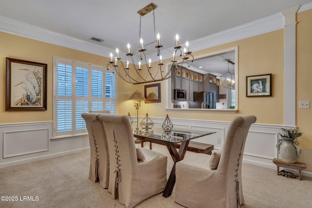 carpeted dining space with a wainscoted wall, visible vents, crown molding, and a decorative wall