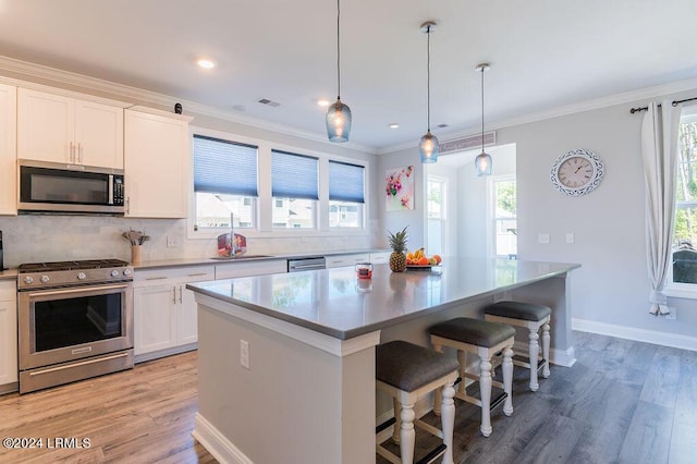 kitchen with decorative light fixtures, white cabinetry, a center island, stainless steel appliances, and light hardwood / wood-style flooring