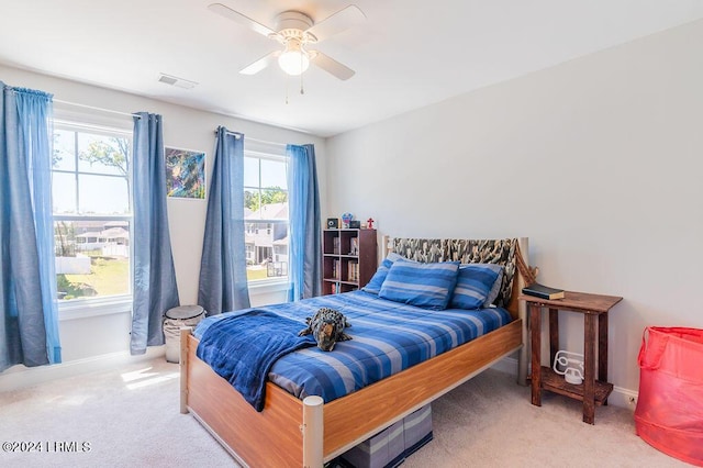 bedroom with multiple windows, ceiling fan, and light carpet