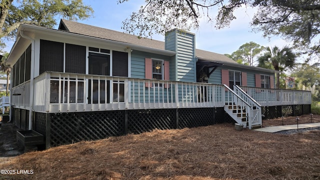 back of house with a chimney, roof with shingles, a deck, and a sunroom