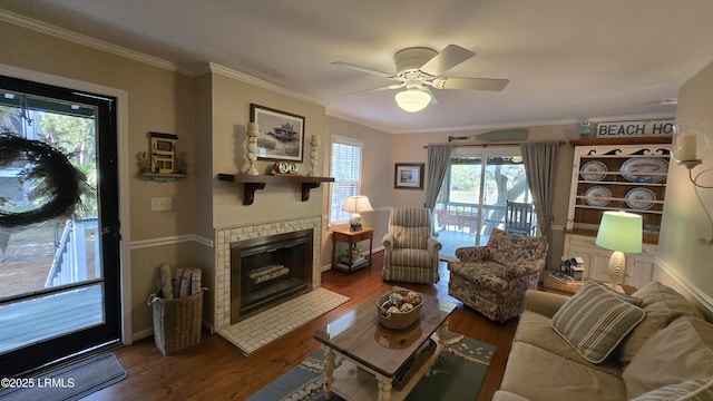 living room featuring a tiled fireplace, crown molding, wood finished floors, and ceiling fan