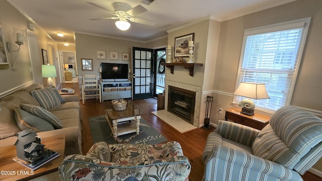 living room featuring a ceiling fan, wood finished floors, baseboards, a tiled fireplace, and crown molding