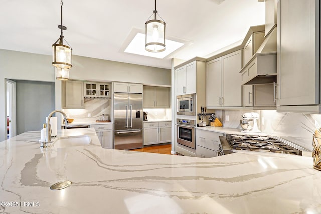 kitchen with built in appliances, a sink, custom exhaust hood, gray cabinetry, and backsplash