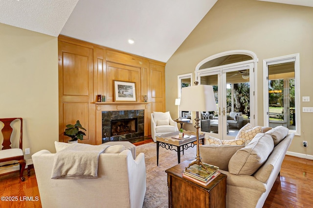 living room with high vaulted ceiling, a premium fireplace, wood finished floors, baseboards, and french doors