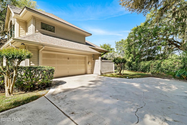 view of side of home featuring a garage, concrete driveway, and roof with shingles