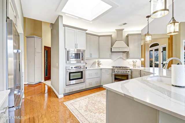 kitchen with visible vents, light wood-style flooring, appliances with stainless steel finishes, a sink, and premium range hood