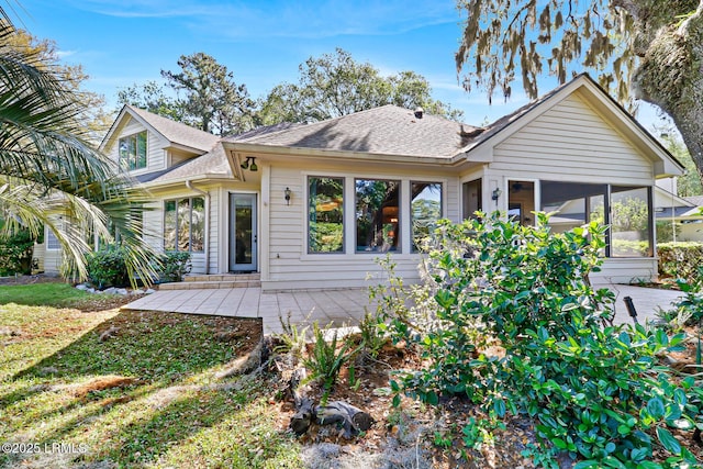 rear view of house featuring a shingled roof, a sunroom, and a patio