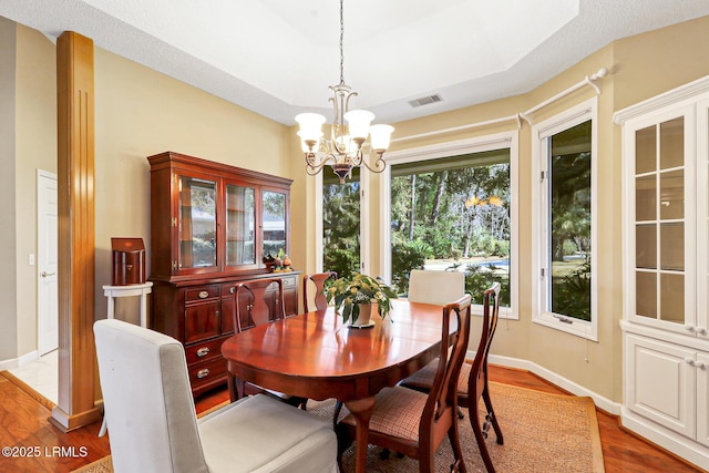 dining area featuring a chandelier, a raised ceiling, visible vents, and wood finished floors