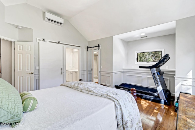 bedroom featuring a wainscoted wall, lofted ceiling, a wall mounted AC, a barn door, and wood finished floors