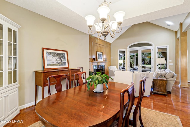 dining space with a notable chandelier, wood finished floors, a high end fireplace, vaulted ceiling, and french doors